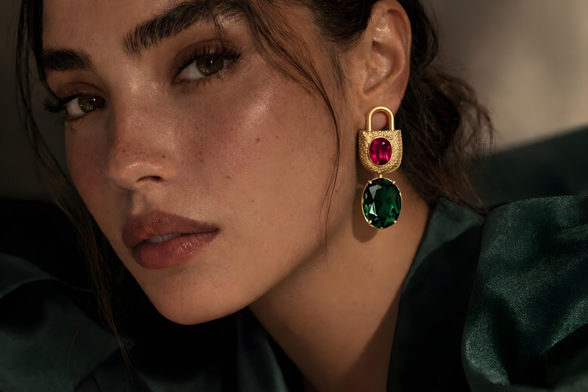 Close-up of a woman wearing gold plated brass earrings with red and green gemstones.