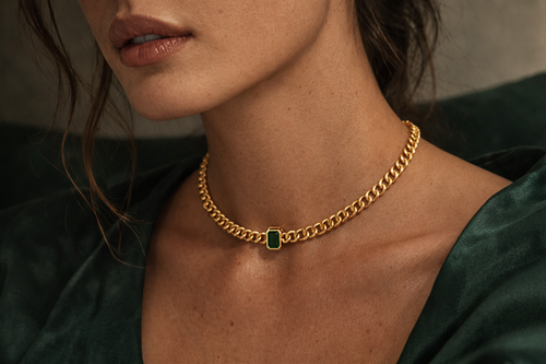Gold  plated brass necklace with a green gemstone on a grey background