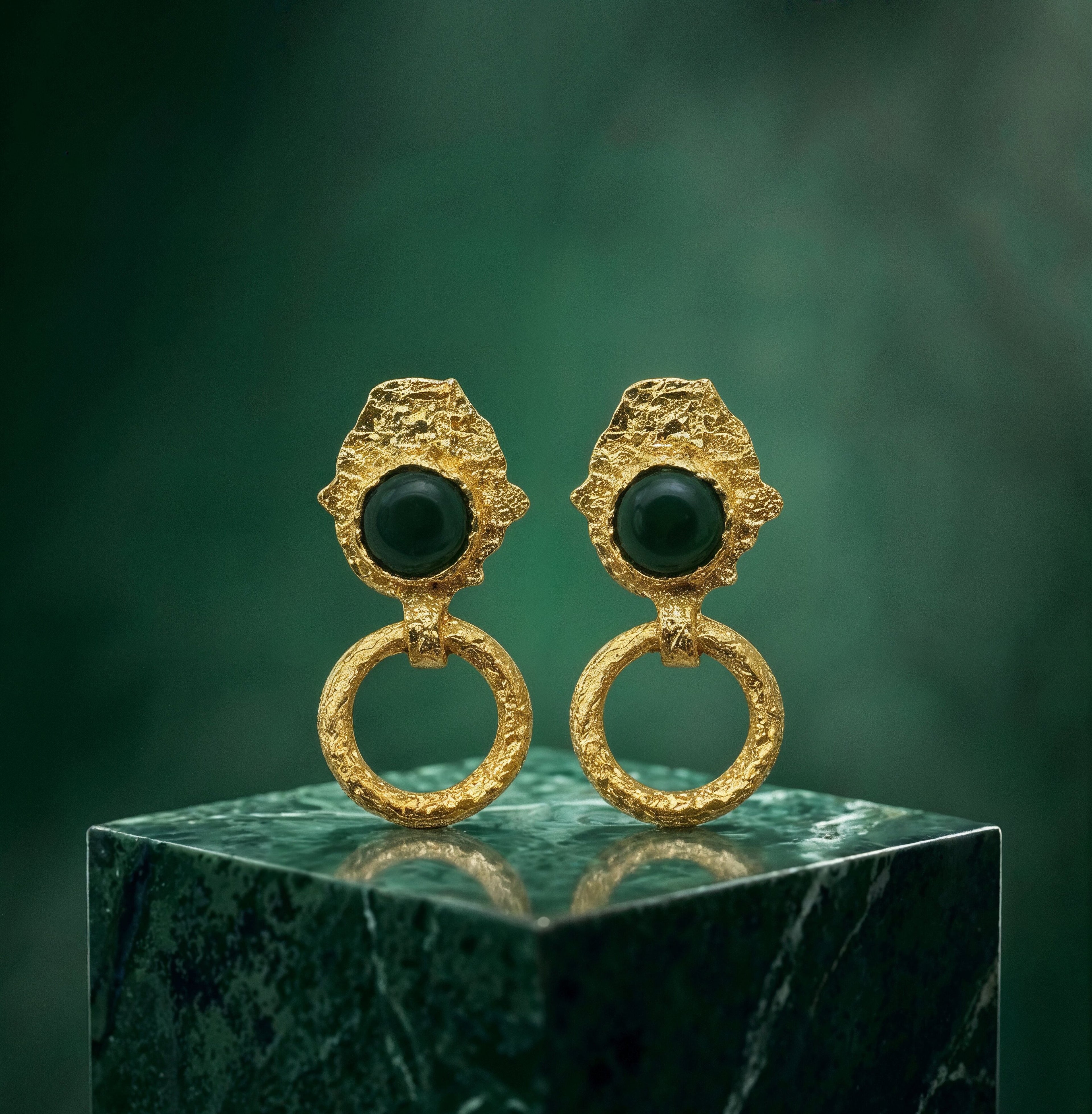 Gold plated brass earrings with green gemstones on a green marble base against a green background