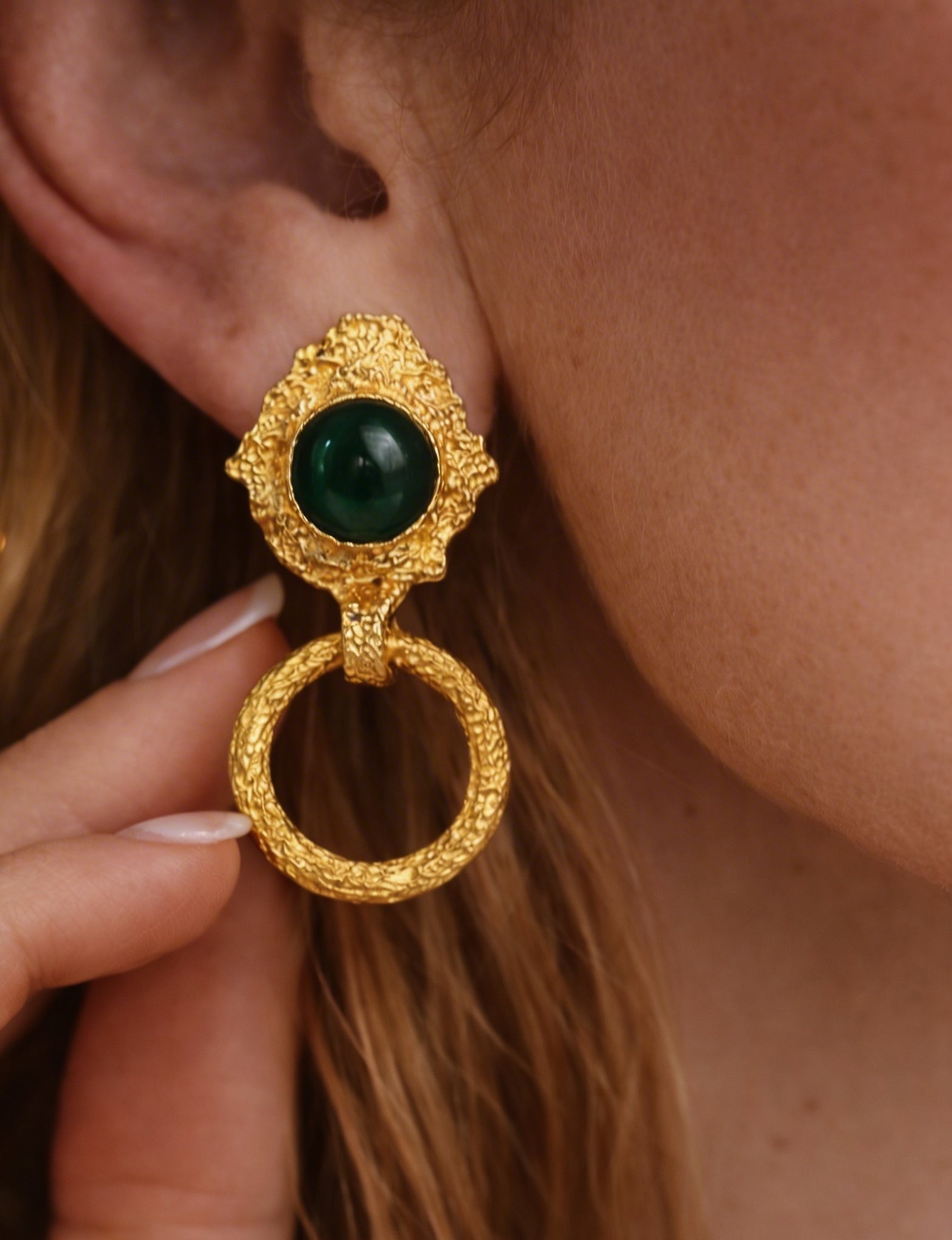 Gold plated brass earring with a green gemstone worn by a woman