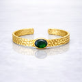 Gold plated brass bracelet with a green gemstone on a person's wrist, wearing a dark green stone.