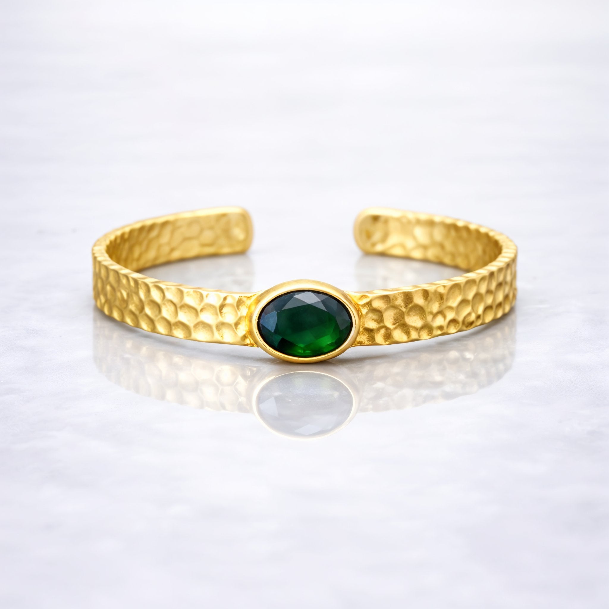 Gold plated brass bracelet with a green gemstone on a person's wrist, wearing a dark green stone.