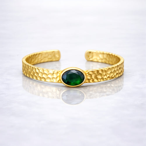 Gold plated brass bracelet with a green gemstone on a person's wrist, wearing a dark green stone.