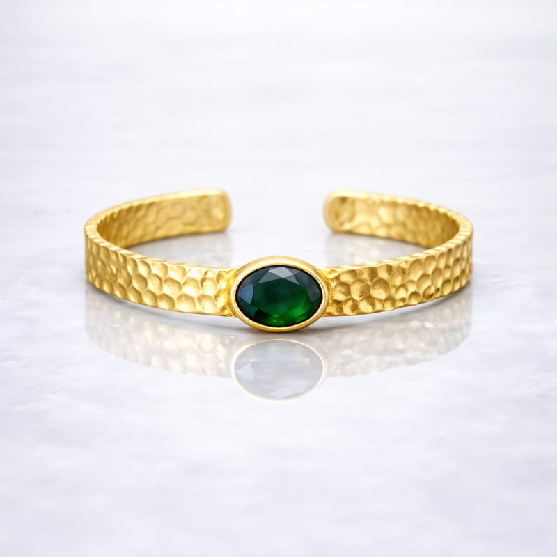 Gold plated brass bracelet with a green gemstone on a person's wrist, wearing a dark green stone.