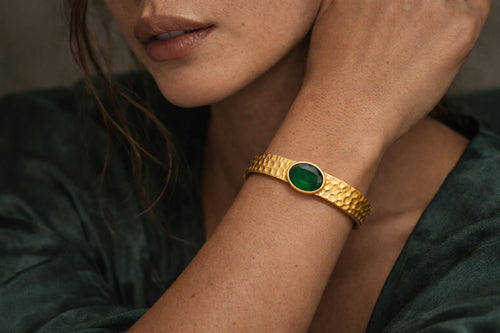 Gold plated brass bracelet with a green gemstone on a person's wrist, wearing a dark green stone.