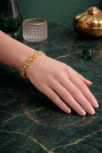 woman hand wearing a gold plated bracelet on a dark green marble surface with decorative items.