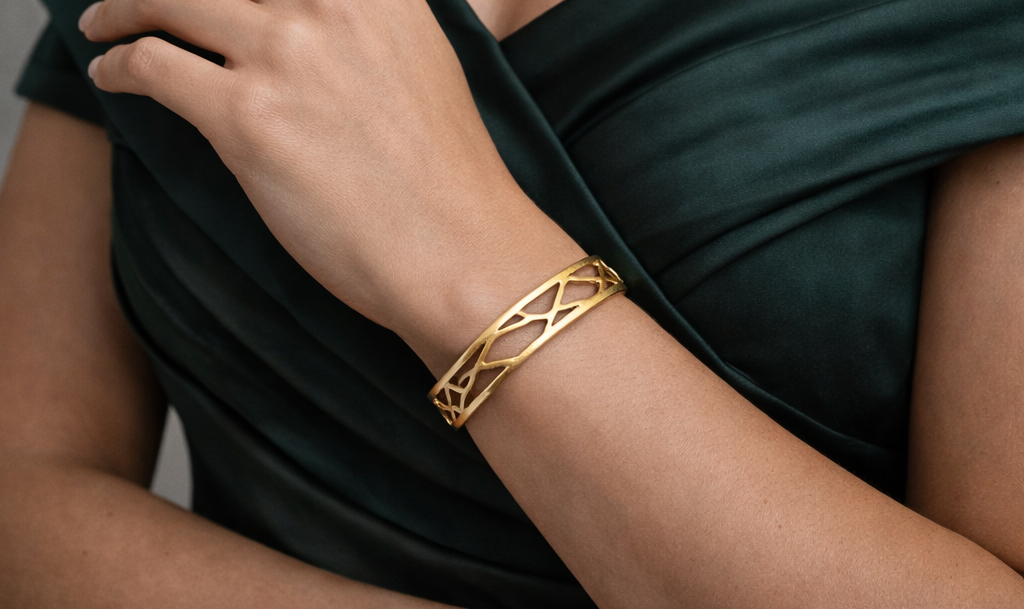 Gold plated brass bracelet on a person's wrist with a dark green dress in the background